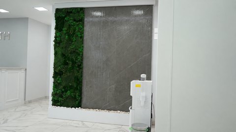 Водопад по серому керамограниту рядом с вертикальной полосой мха и кулером